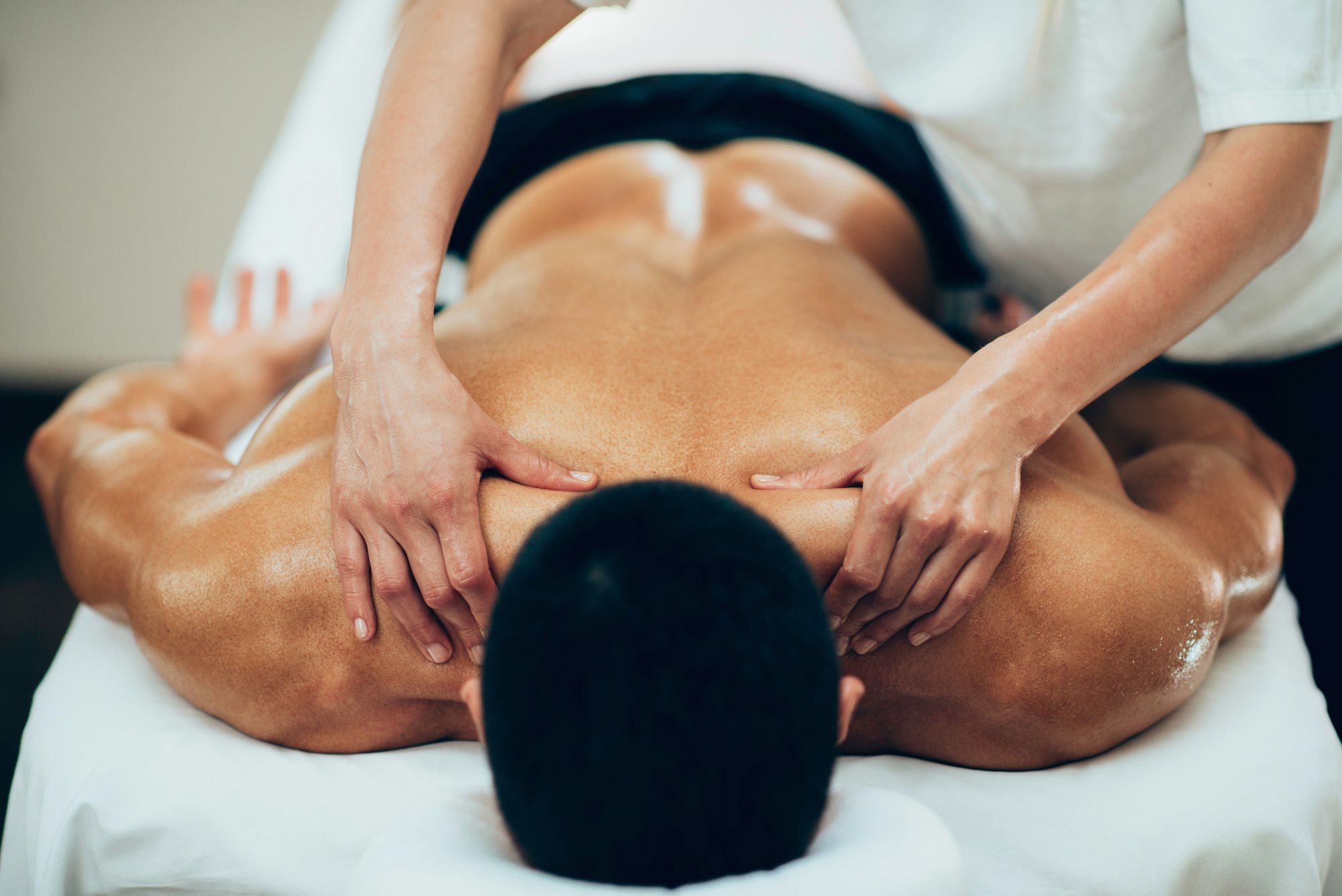 Pilates Canal Madrid Una persona recibe un masaje de espalda mientras está tumbada boca abajo en una camilla de masajes. Las manos del masajista se colocan sobre la parte superior de la espalda y los hombros de la persona, aplicando presión. El individuo sin camiseta disfruta de una escena tranquila y relajante, perfecta para Readaptación Deportiva en Madrid.