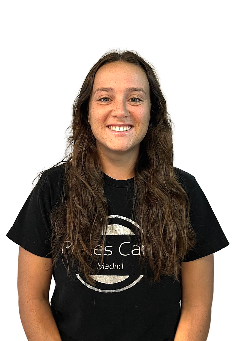Pilates Canal Madrid Una persona con cabello castaño largo y ondulado sonríe y mira hacia delante. Lleva una camiseta negra con un texto blanco que dice "Centro de bienestar en Madrid". El fondo es blanco liso.